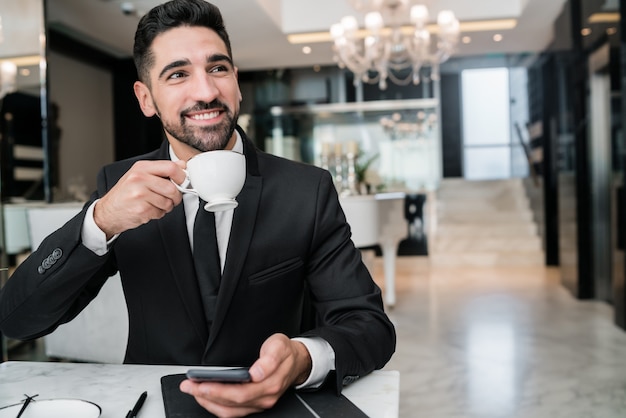 仕事を休んでホテルのロビーでコーヒーを飲む青年実業家の肖像画。出張と旅行のコンセプト。