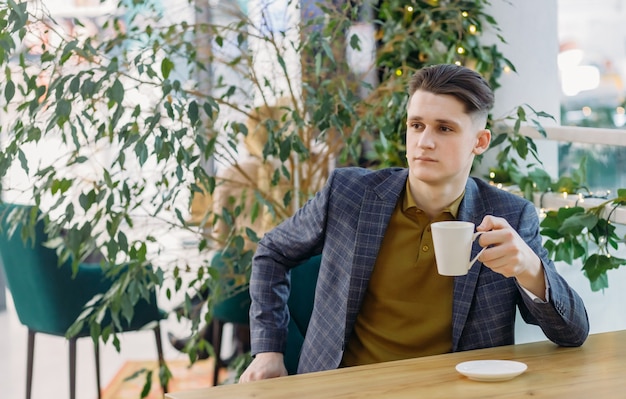 Photo portrait of a young businessman in a cafe with a cup of coffee in his hands.
