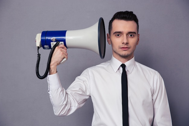 Portrait of a young businessman holding loudspeaker on gray wall