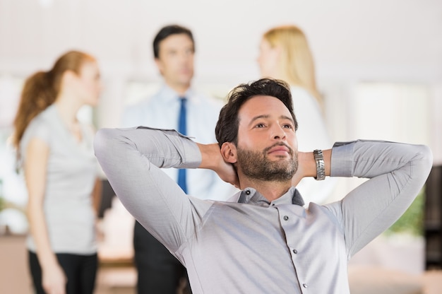 Portrait of a young businessman relaxing with hands behind head in office.