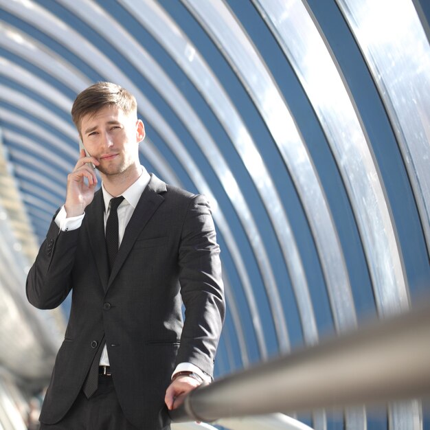 Portrait of a young businessman in suit standing at office and talking by phone