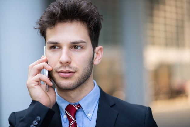 Portrait of a young businessman talking on the phone outdoors in front of his office