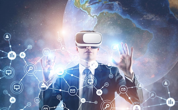 Portrait of a young businessman wearing a suit and VR glasses and interacting with what he sees. A global network background. Elements of this image furnished by NASA Toned image double exposure