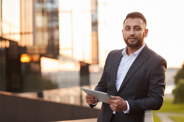 Portrait of young businesswoman in formal suit looking at camera while using digital tablet in the city