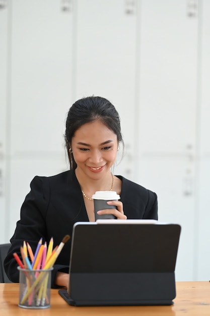 Portrait of young businesswoman sitting working with computer tablet and drinking hot coffee