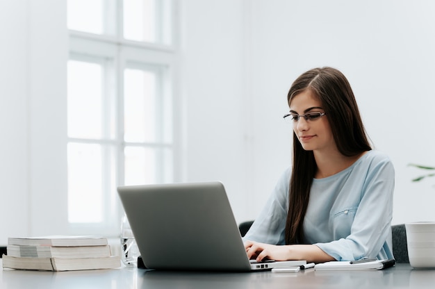 Portrait of young businesswoman typing on laptop while sitting at her workplace 