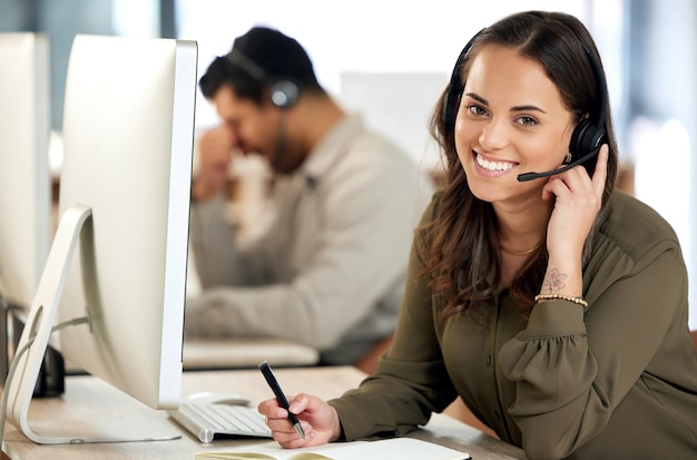 Portrait of a young businesswoman using a headset and writing in a notebook in a modern office