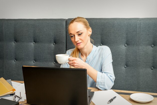 Портрет молодой деловой женщины, использующей ноутбук, сидя за столом с чашкой кофе в кафе