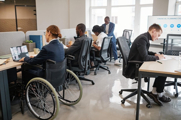 Portrait of young businesswoman using wheelchair in office and smiling at camera, copy space