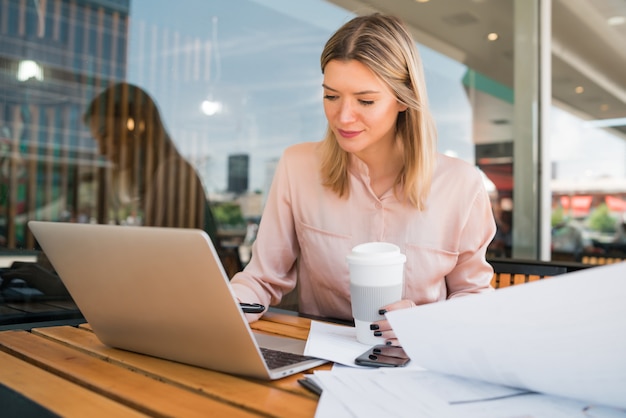 コーヒーショップで彼女のラップトップに取り組んでいる若い実業家の肖像画。ビジネスコンセプト。