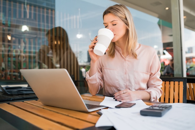 コーヒーショップで彼女のラップトップに取り組んでいる若い実業家の肖像画。ビジネスコンセプト。