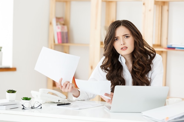 Portrait of young businesswoman working in her office with serious facial expression with document report