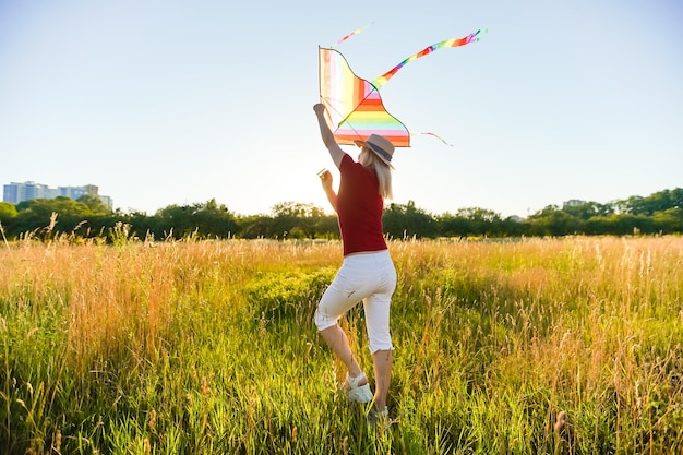 Portrait of a young and carefree woman launching kite on the greenfield. Concept of active lifestyle in nature