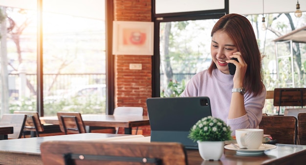 Portrait of young casual businesswoman using mobile phone and tablet computer smilling with successful business while sitting at cafe