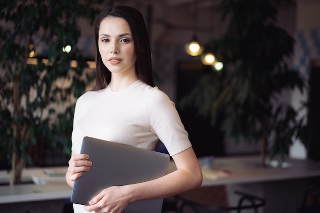 Portrait of young casual woman holding laptop