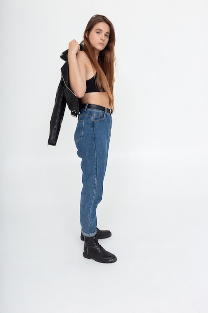 Portrait of young caucasian attractive woman with long brown hair in blue jeans and black leather jacket on white background. skinny pretty lady posing at studio