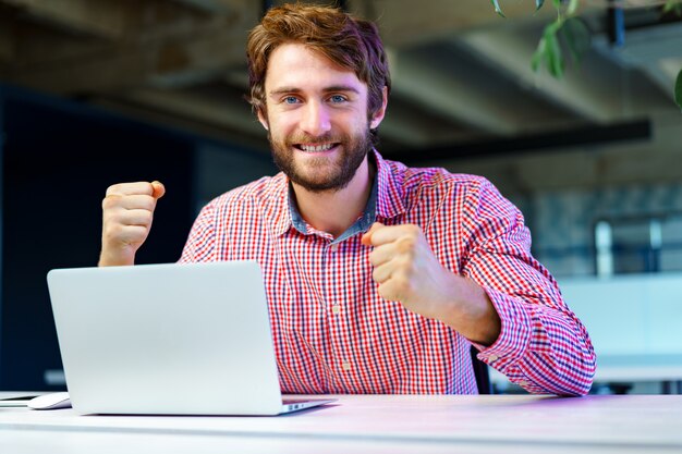 Portrait of young caucasian businessman using laptop computer at his workplace in modern office