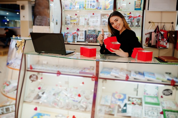 Portrait of young caucasian female woman seller hold red gift boxes. Small business of candy souvenirs shop.