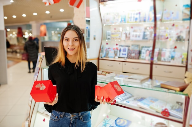 Портрет молодой кавказской женщины продавец держит красные подарочные коробки. Малый бизнес кондитерского магазина сувениров.
