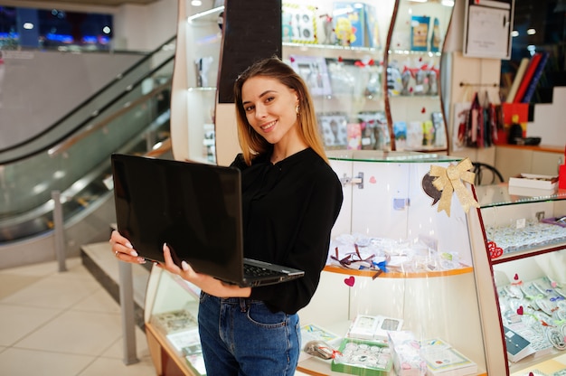 ラップトップを使用して若い白人女性販売者の肖像画。キャンディのお土産屋の中小企業。