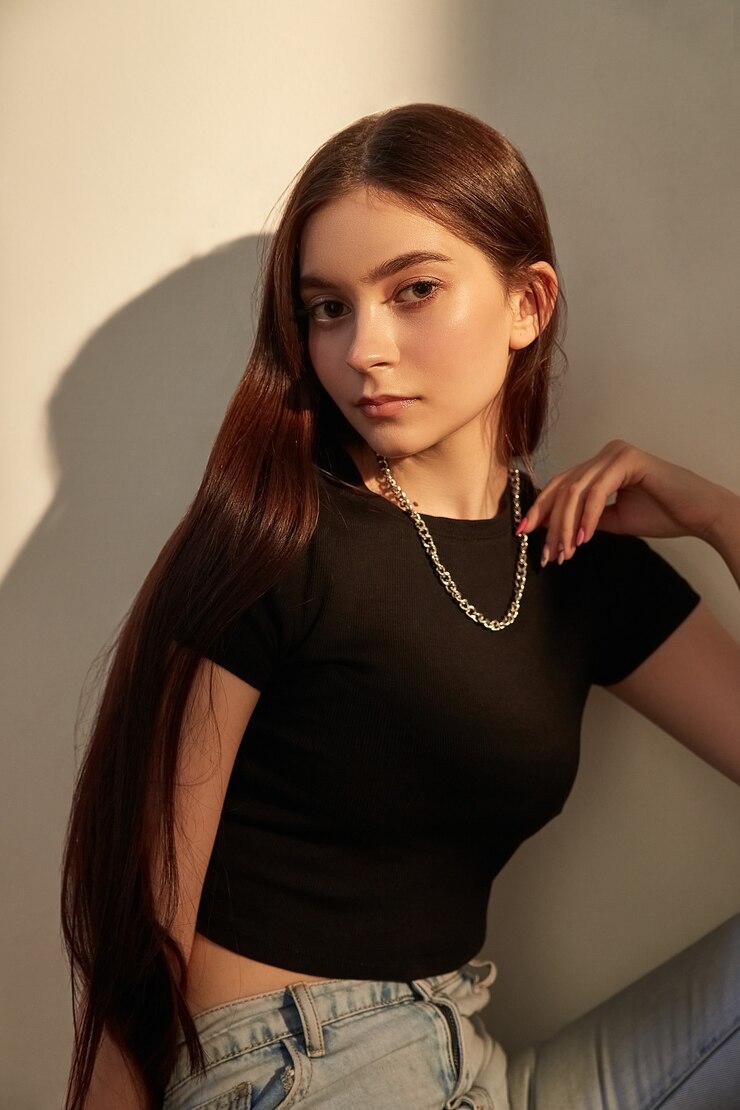 Photo 壁の横に座っているジーンズの長い髪の若い白人の女の子の肖像画
