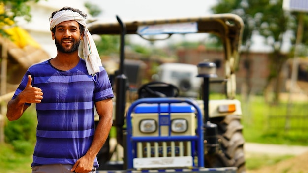 Portrait of young Caucasian handsome man farmer standing on the road in field and smiling to camera Big tractor on background Male worker in agricultural farm Agriculture farming