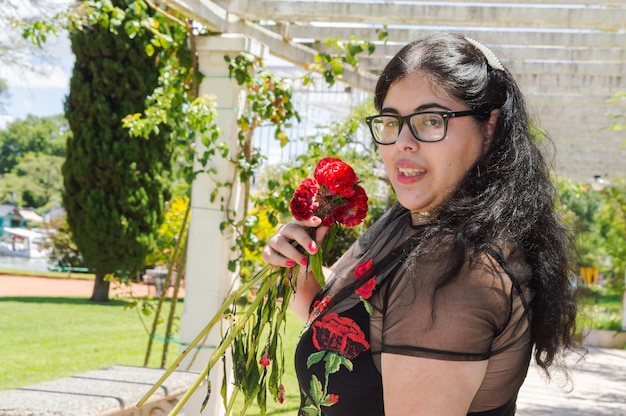 Portrait of young caucasian hispanic latin plus size woman in a public park smiling with flowers