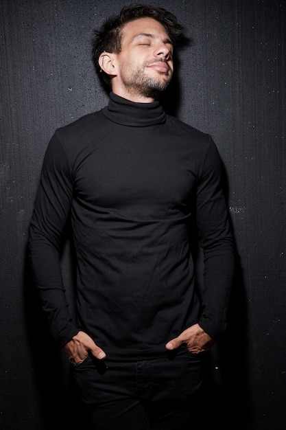 Portrait of a young Caucasian man with brown hair wearing a black turtleneck shirt Posing on black background Ear piercing