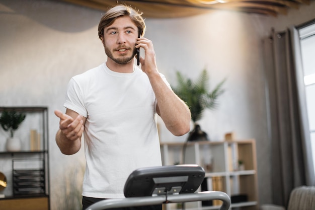 Portrait of young caucasian sportive man in sportswear talking on smartphone