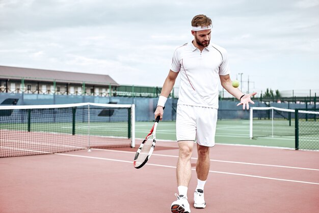 Ritratto di giovane giocatore caucasico adolescente che indossa abiti da tennis camminando sul campo da tennis estivo hard