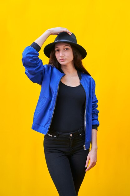 Portrait of a young caucasian woman in black hat and blue jacket, holding hat with hand