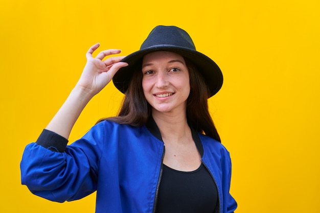 Portrait of a young caucasian woman in black hat and blue jacket, holding hat with hand