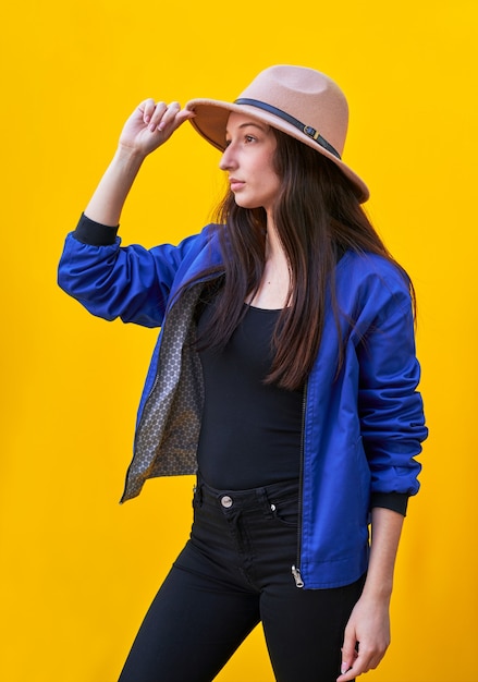 Portrait of a young caucasian woman in black hat and blue jacket, holding hat with hand