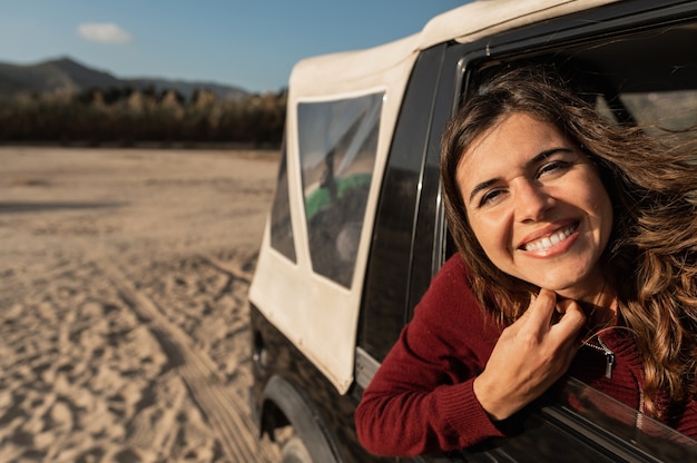 Portrait of young caucasian woman looking at the camera smiling. Female looking out car window. off-road vehicle in sandy road during a journey.