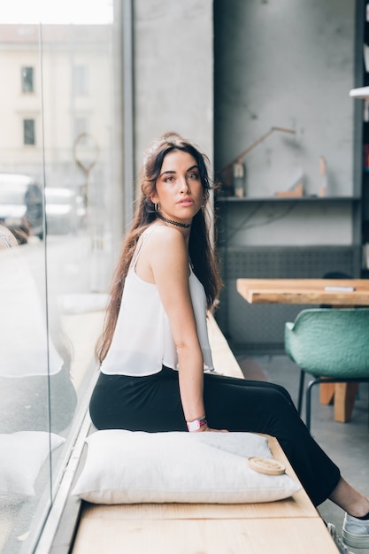 Portrait of young caucasian woman sitting and looking camera in bright apartment 