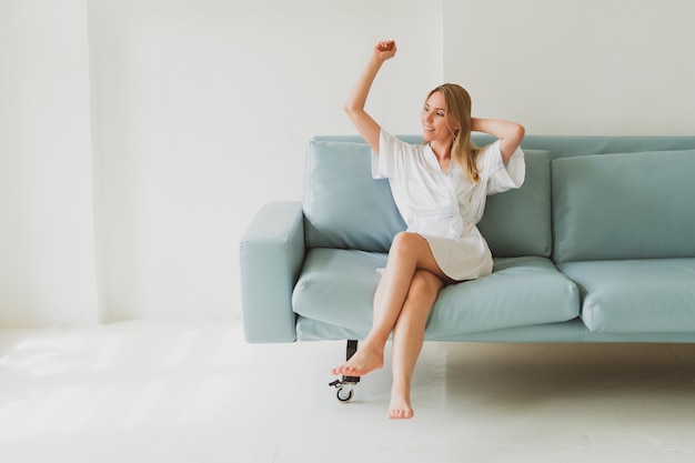 Portrait of a young charming woman in a silk robe at home on the sofa