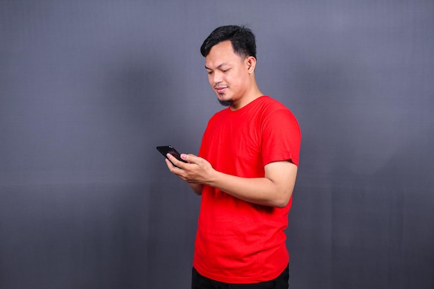 Portrait of a young cheerful asian man using mobile phone isolated over gray background,