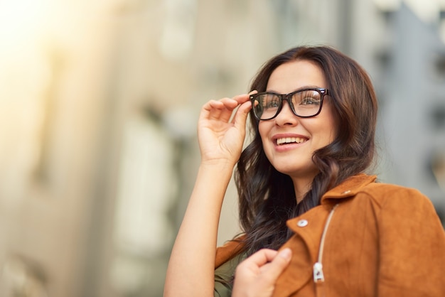 Photo portrait of a young cheerful business woman adjusting her eyeglasses and looking aside while