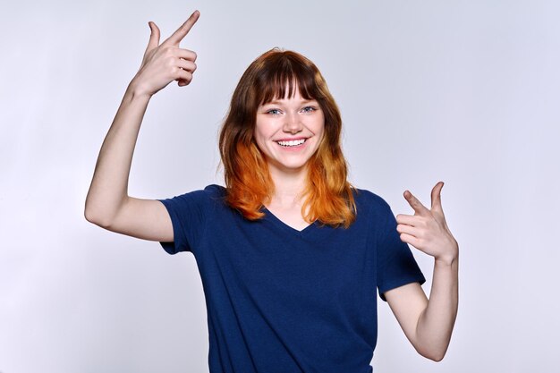 Portrait of young cheerful female with red hair on light studio background