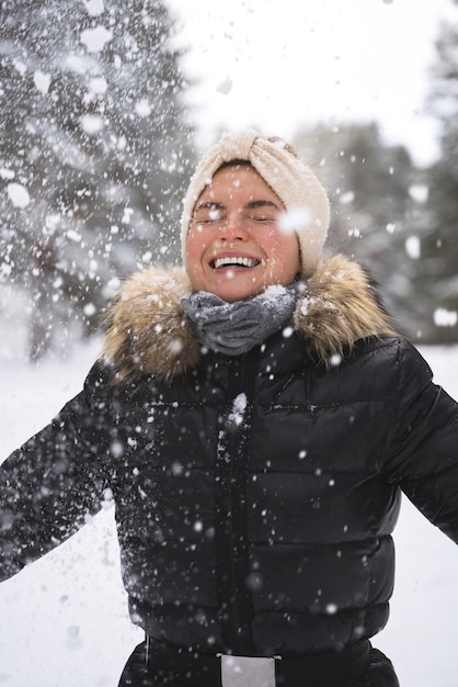 Portrait of young cheerful girl enjoying snowfall during beautiful winter day
