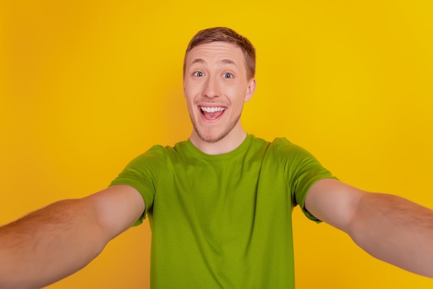 Портрет молодого веселого человека с счастливой позитивной улыбкой, делающей селфи, изолированным на желтом цветном фоне