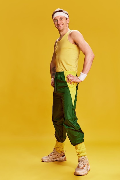 Portrait of young cheerful man in sports uniform posing over bright yellow studio background Concept of emotions lifestyle sport