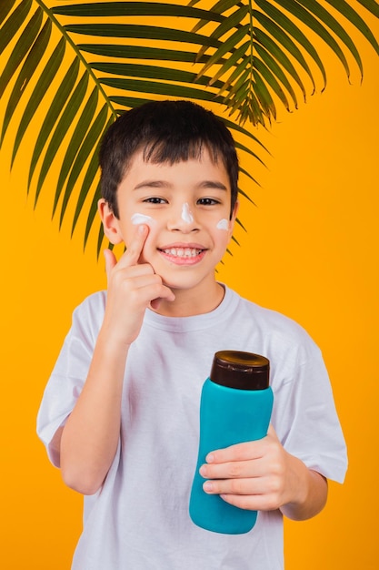 Portrait of a young child putting on sunscreen on a yellow background.