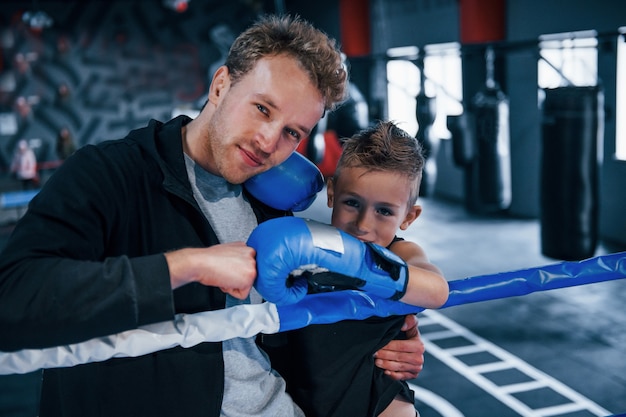 Portrait of young coach with little boy standing in the boxing ring.