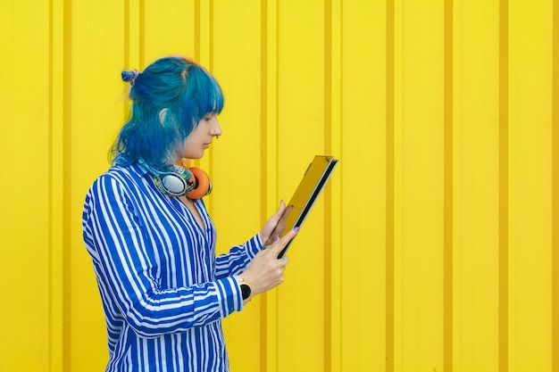 Portrait of a young colored girl holding laptop computer isolated on yellow