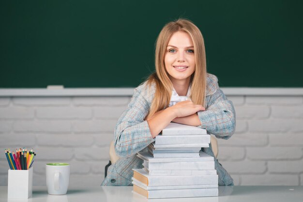 Portrait of a young confident and attractive female student studying in school classroom Cute student girl with books on blackboard background with copy space