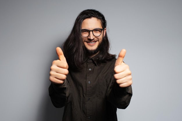 Portrait of young confident attractive man with long hair gesturing thumbs up