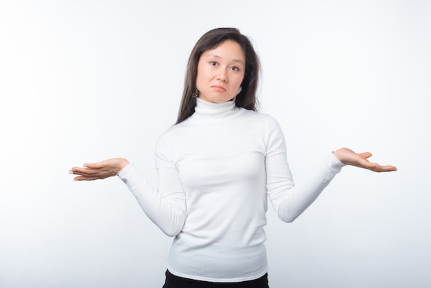 Portrait of young confused woman standing over white wall