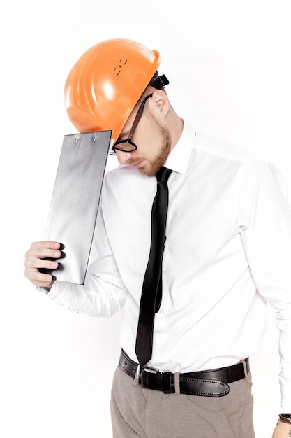 白い背景の上のフォルダーとオレンジ色のヘルメットの若い建設エンジニアの肖像画