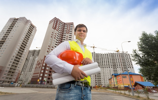 ヘルメットを保持している安全ベストの若い建設エンジニアの肖像画